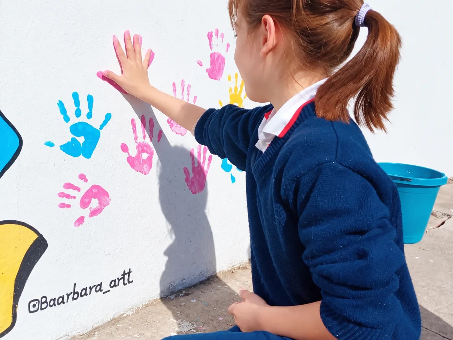 Una alumna apoya la mano pintada sobre la pared del mural