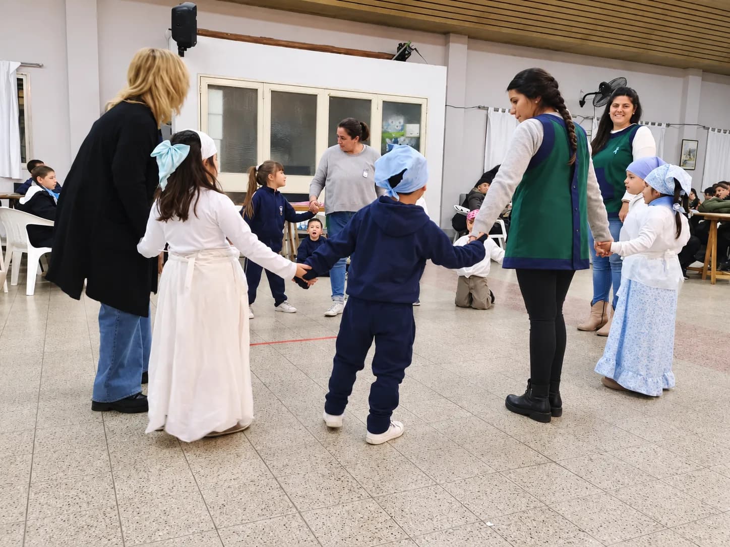 Alumnos y maestras bailando en ronda en el salón